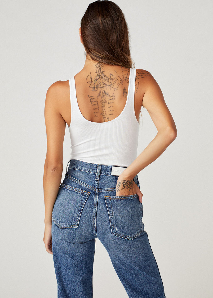 Brunette model with back tattoo wearing the Brittaney tank suit in white by Clyque and blue jeans showing the open back feature.