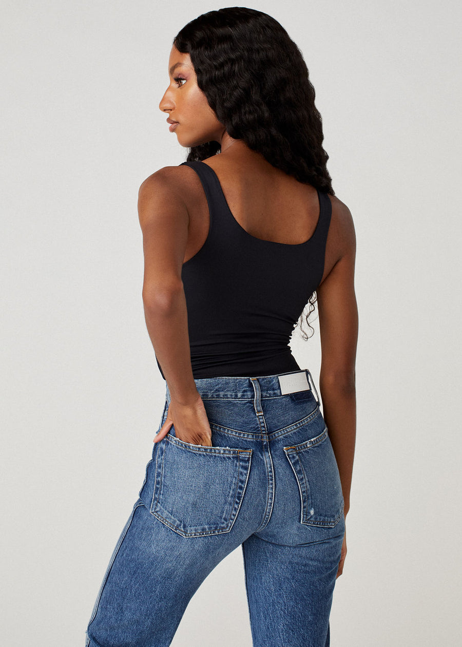 Model back facing the camera wearing high waisted blue jeans and the Sheera bodysuit in black.