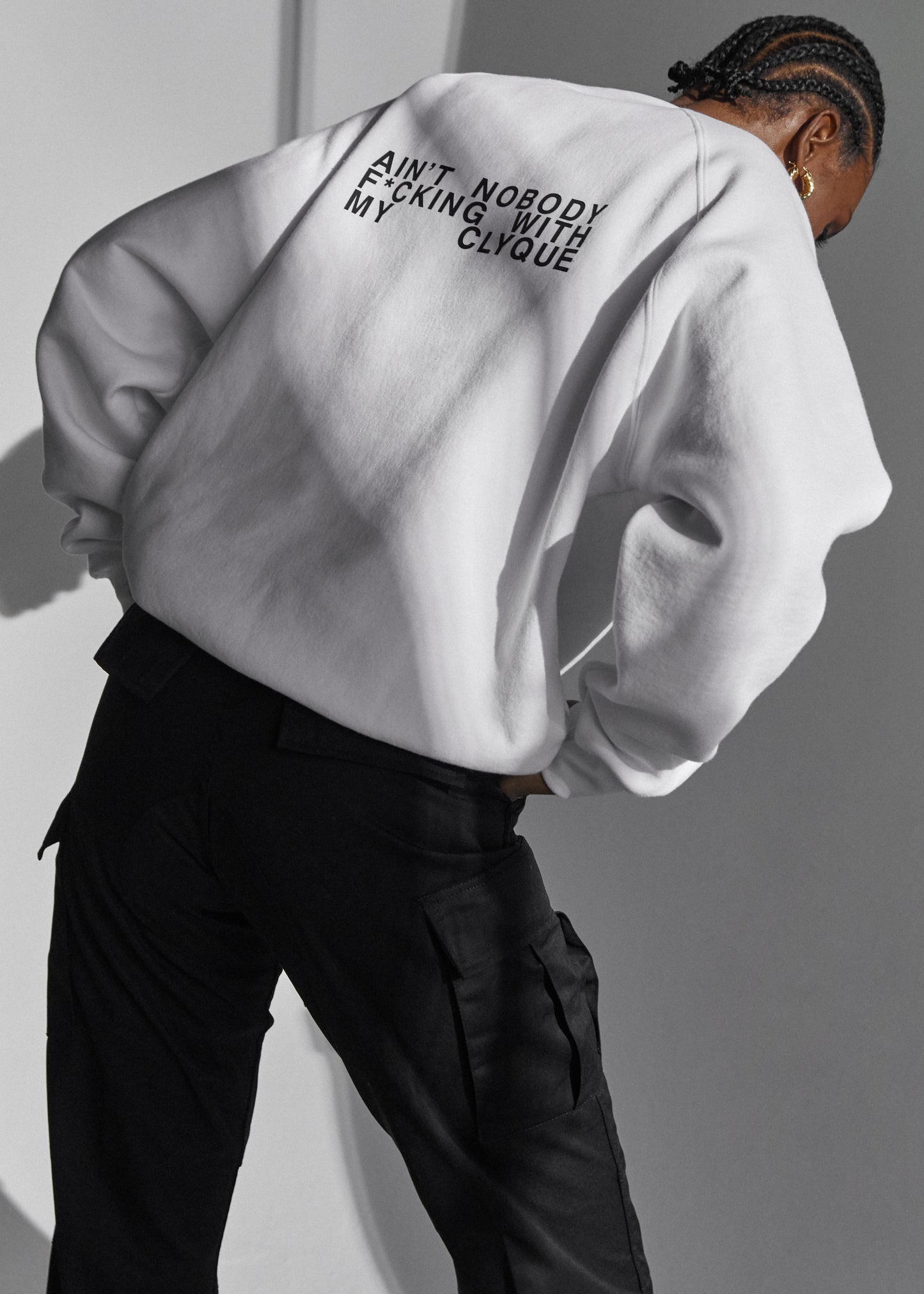 Model wearing the white over-sized sweatshirt by Clyque with a graphic on the back .