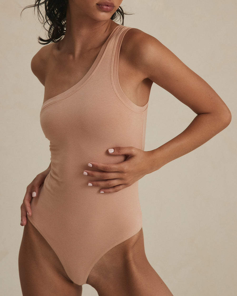 Model posing in an one shoulder strap bodysuit from Clyque in blush hue.  