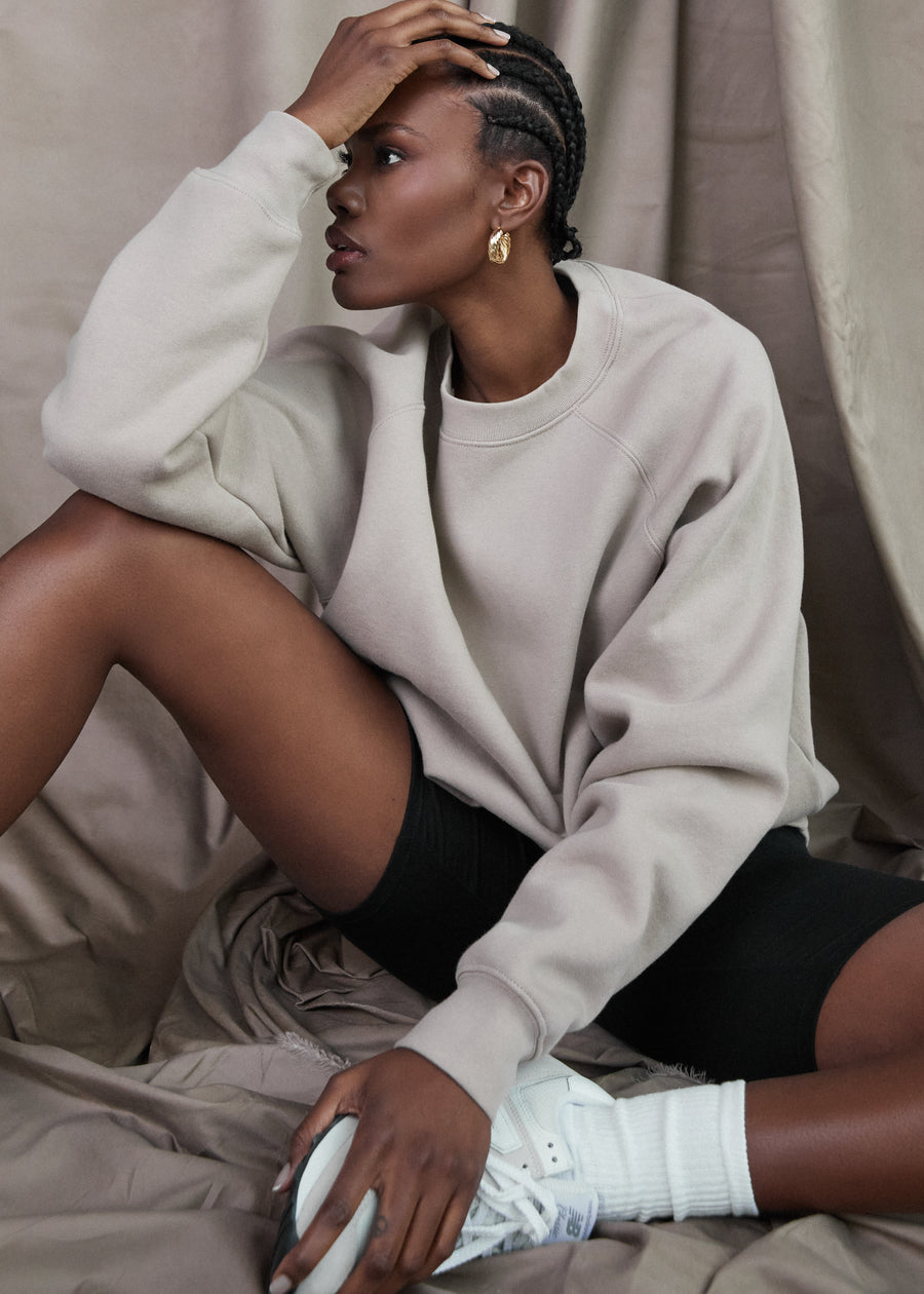 Model sitting on the floor in a studio wearing the Clyque List sweatshirt in colour greige.